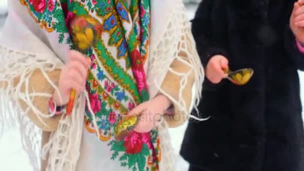 Dos niñas pequeñas en ropa y pañuelos de estilo ruso juegan en cucharas de madera contra el fondo de la nieve — Vídeo de stock
