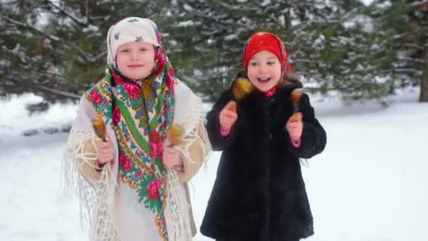 Two small girls in clothes and kerchiefs in Russian style play on wooden spoons against the background of snow — Stock Video