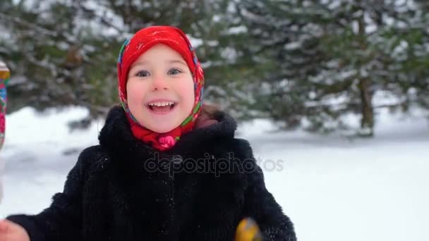 A little girl in a fur coat and in a red scarf in Russian style plays on wooden spoons — Stock Video