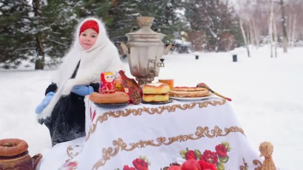 Una niña pequeña en un abrigo de piel y una bufanda en estilo ruso se sienta en una mesa festiva y juega una matryoshka rusa — Vídeo de stock