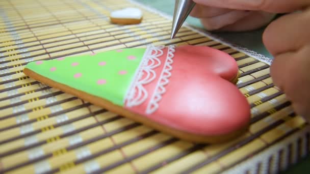 Woman confectioner decorates and decorates the glaze with gingerbread cookies in the shape of heart. — Stock Video