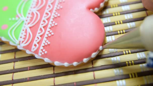 Woman confectioner decorates and decorates the glaze with gingerbread cookies in the shape of heart. — Stock Video