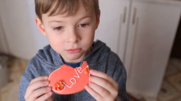 Boy eating a gingerbread in the shape of a heart with the inscription "love" — Stock Video