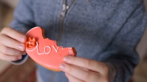 Niño comiendo un pan de jengibre en forma de corazón con la inscripción "amor " — Vídeo de stock