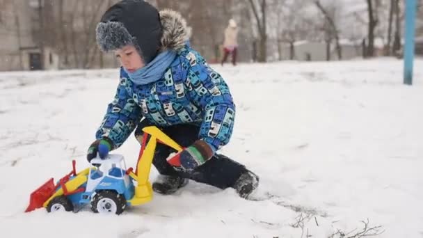 Kind jongen spelen in een speelgoedauto - een trekker in de sneeuw. — Stockvideo