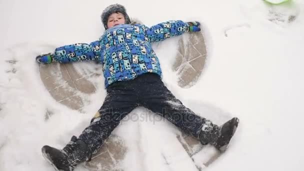 Мальчик делает ангела на снегу — стоковое видео