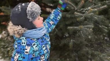 şirin bebek çocuk kış giysileri ve bir şapka kar ve bir Noel ağacı arka planı.
