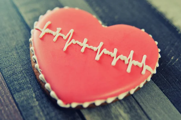 Lebkuchen in Herzform mit roter Glasur und einem Muster in Form eines Kardiogramms auf hölzernem Hintergrund. — Stockfoto