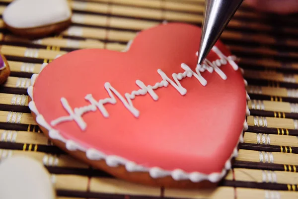 a female pastry cooks a glaze with a cardiogram on a gingerbread in the form of a heart.
