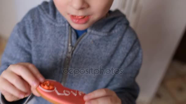 Niño comiendo un pan de jengibre en forma de corazón con la inscripción "amor " — Vídeos de Stock