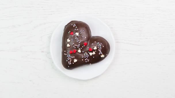 Manger un délicieux dessert - un cœur de chocolat en gros plan sur une assiette blanche sur un fond blanc en bois . — Video