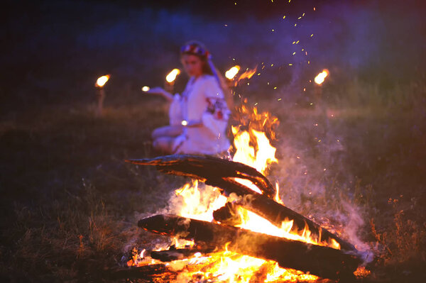 Украинка с венком из цветов на голове на фоне огня
