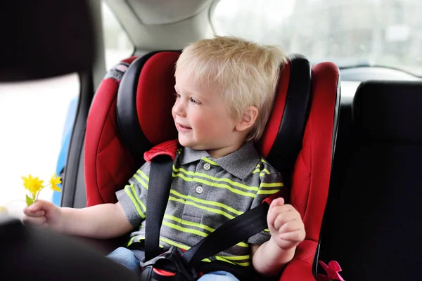 Portrait of a young child of a boy with blond hair in a childrens car seat. — Stock Photo, Image