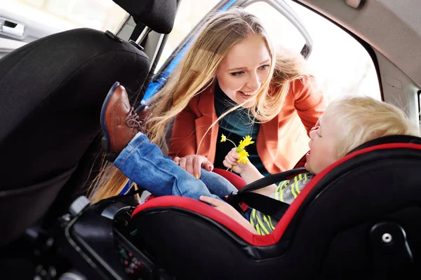 Mamá pone al niño en el asiento del coche y se abrocha los cinturones de seguridad . —  Fotos de Stock