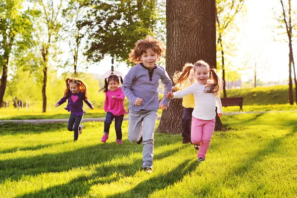 Tanti bambini piccoli che sorridono correndo lungo l'erba del parco . — Foto Stock