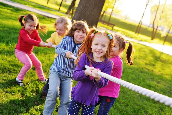 En grupp av små förskolebarn spela en dragkamp i parken. — Stockfoto