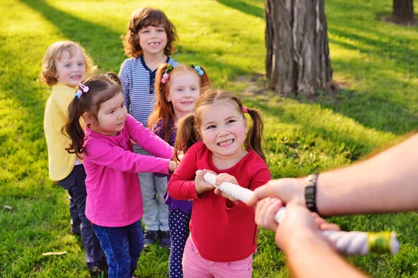 Un grupo de niños preescolares pequeños juegan un tirón de la guerra en el parque . —  Fotos de Stock