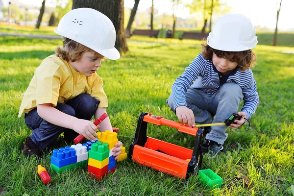 Niños en cascos de construcción blancos juegan en trabajadores con herramientas de juguete . — Foto de Stock