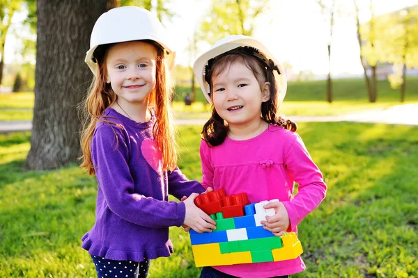 Niñas lindas en cascos de construcción blancos jugando en los niños diseñador en el parque — Foto de Stock