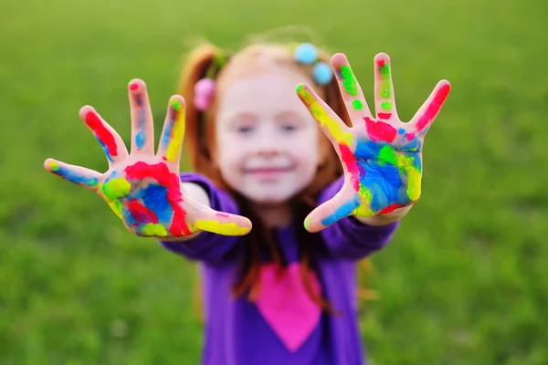 Menina com cabelo vermelho mostra suas mãos sujas com tintas multicoloridas e sorrisos — Fotografia de Stock