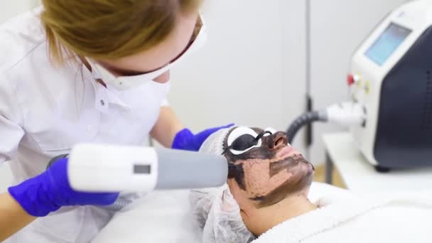 Jovem sobre o procedimento de descascamento de carbono no fundo da sala de cosmetologia moderna. Cosmetologia a laser — Vídeo de Stock