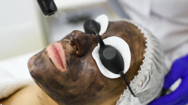 Mujer joven en el procedimiento de peeling de carbono en el fondo de la sala de cosmetología moderna. Cosmetología láser — Vídeo de stock