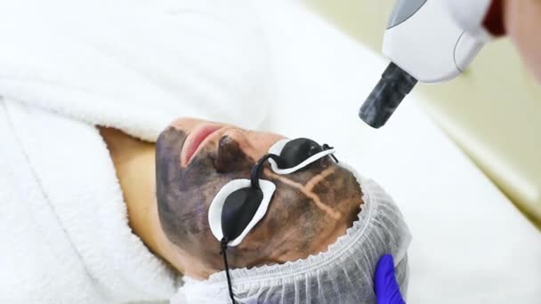 Mujer joven en el procedimiento de peeling de carbono en el fondo de la sala de cosmetología moderna. Cosmetología láser — Vídeo de stock