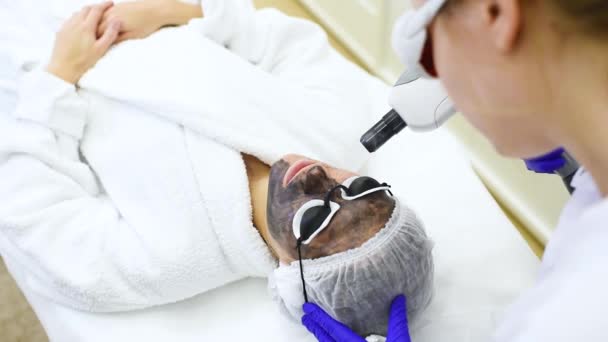 Mujer joven en el procedimiento de peeling de carbono en el fondo de la sala de cosmetología moderna. Cosmetología láser — Vídeo de stock