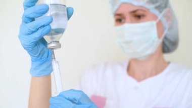 Genç bir kadın doktor ya da hemşire şırıngayı iğne için sıvıyla doldurur..