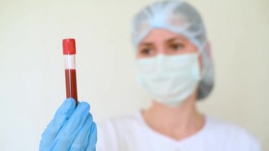 Kadın doktor ya da hemşire üzerinde kan örneği olan bir tüp tutuyor..