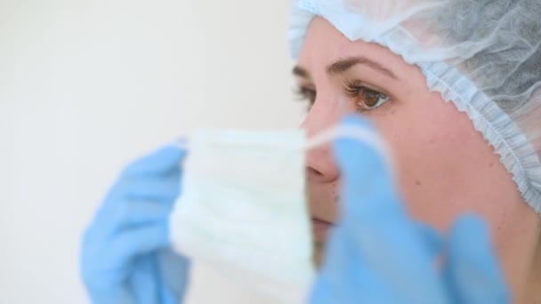Jonge vrouwelijke arts of verpleegkundige zet een medisch beschermend masker op een witte achtergrond. Coronavirus, epidemie, pandemie, covid-19 — Stockvideo