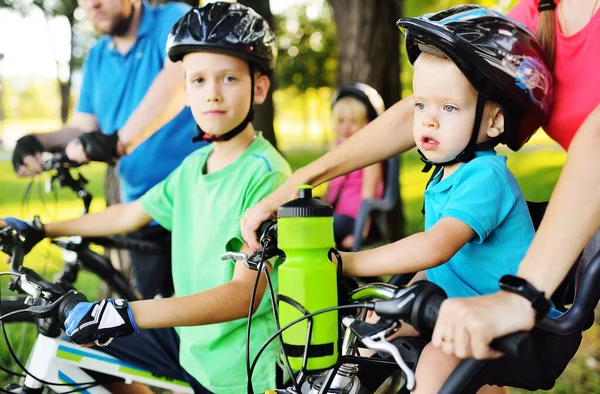 Small child a boy in equipment and a helmet sits in a childrens Bicycle seat near his parents against the background of the Park and nature — Stock Photo, Image