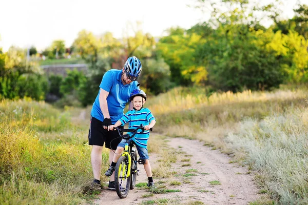 father teaches a small child of a son in a protective helmet to ride a Bicycle.