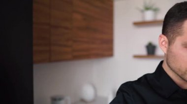 Evden çalışan genç iş adamının videosunu yavaşlat. Mutfakta sıcak kahve ya da çay içmek. Videoda kendine güvenen başarılı iş adamı.