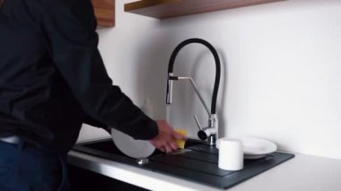 İş dünyasındaki adamın videosu musluğu açar ve bulaşıkları ya da beyaz tabakları süngerle temizlemeye başlar. Kamera soldan sağa hareket ediyor. Öğle yemeğinden sonra tabakları temizliyorum..