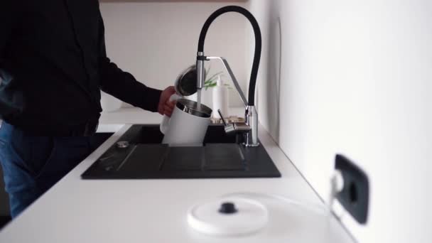 Βιντεοδιαδικασία του τύπου να ανοίγει τη βρύση και να ρίχνει νερό μέσα. Κλείσ 'το και βάλε ηλεκτρικό βραστήρα για θέρμανση. Έξυπνος βραστήρας που δουλεύει από το τηλέφωνο. Guy παίρνει smartphone από την τσέπη. — Αρχείο Βίντεο