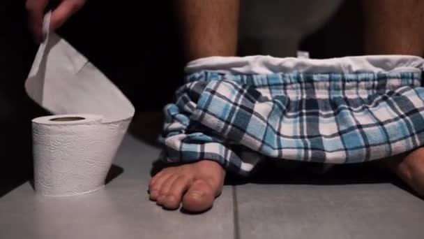 男子排便后手摸到卫生纸滚筒并将其剪断的视频过程。那家伙脚上穿着裤子，坐在卫生间的锅子里。一个人在厕所或厕所里靠近点. — 图库视频影像