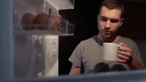 Hombre hambriento abriendo refrigerador. Mira dentro. Sostenga la taza de bebida en las manos. Cerrar la nevera y no tomar comida de ella. Medianoche robando comida . — Vídeos de Stock