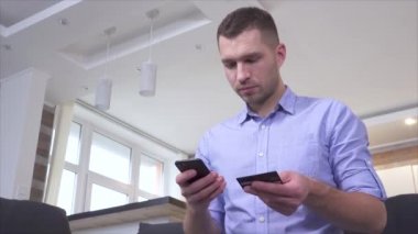 Genç adam kredi kartını cep telefonuyla ödeme yapmak için kullanıyor. Karttan akıllı telefon hesabına para yollamak. Mutlu olumlu adam işlemden memnun..