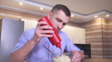 Mutfaktaki genç adamın videosu. Makarnaya biraz ketçap ekle ve çatalla karıştır. Yemek için lezzetli yemekler hazırlayın. Yemek zamanı..