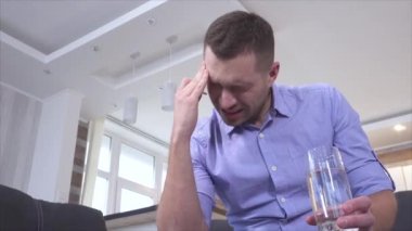 Genç adam akşamdan kalma ya da baş ağrısı çekiyor. Tek başına otur ve beyaz tableti bir bardak suya koy. Ağrı kesici ve insan için rahatlama. Acı sona erdi..