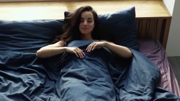 Mladá žena zůstane během karantény doma. Ležel na posteli pod plátěným blaketem a s potěšením se protáhl. Krásné ráno v pokoji. — Stock video