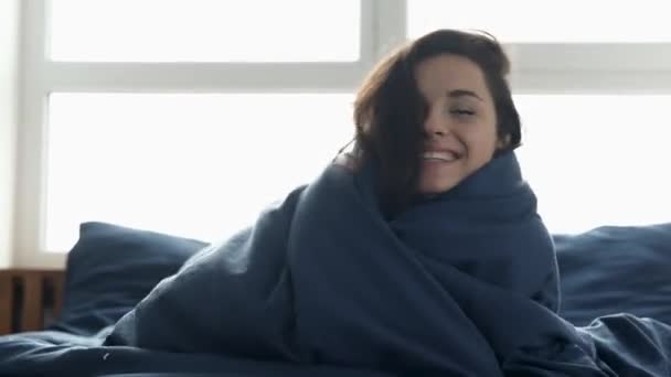 La giovane donna rimane a casa durante la quarantena. Positivo bella ragazza attraente avvolto in coperta di lino e sorriso. Donna allegra godere di trascorrere del tempo in camera da letto al mattino . — Video Stock