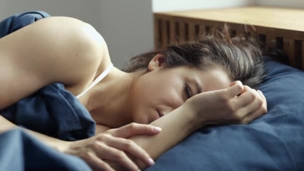 Młoda kobieta zostaje w domu podczas kwarantanny. Nieszczęśliwa nieprzyjemna dziewczyna leżąca na łóżku i zakrywająca twarz przed hałasem lub porannym światłem. Czas wstawać.. — Wideo stockowe