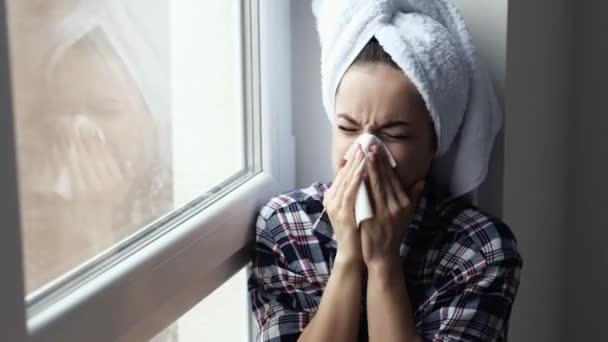 La giovane donna rimane a casa durante la quarantena. Siediti alla finestra dopo il bagno o la doccia. Starnutisce nel tessuto bianco e beve medicine. Soffri di malattia . — Video Stock