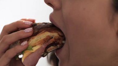 Genç kadın karantina sırasında evde kalıyor. Yaklaş ve et ve sosla yağlı burger yiyen bir kızın görüntüsünü kes. Beyaz arka planda izole edilmiş. Yavaş çekim.