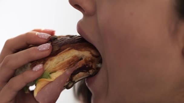 Una joven se queda en casa durante la cuarentena. Cerrar y cortar la vista de la chica comiendo hamburguesa grasa con carne y salsa. Aislado sobre fondo blanco. Movimiento lento . — Vídeo de stock