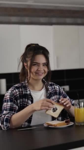 Mujer joven en la cocina durante la cuarentena. Chica alegre juguetona posando con pedazo de pan con agujero en medio de ella. Diviértete solo en apartamento . — Vídeos de Stock