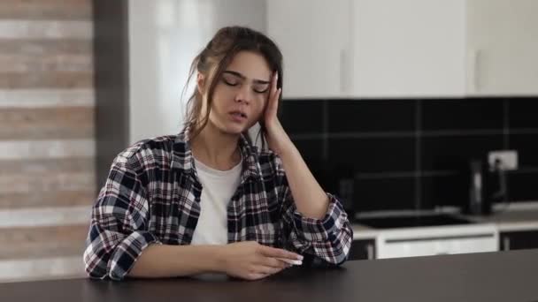 Mladá žena v kuchyni během karantény. Sedni si ke stolu a kýchni do bílé tkáně. Trpí bolestí hlavy. Nemocná dívka na pokoji. — Stock video