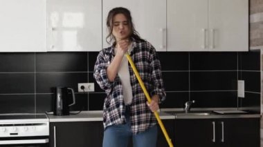 Karantina sırasında mutfakta genç bir kadın. Paspası eline al ve şarkı söyle. Evde mikrofon tutuyormuş gibi yapıp tek başına dans ediyorsun. Ağır çekimde iyi eğlenceler..